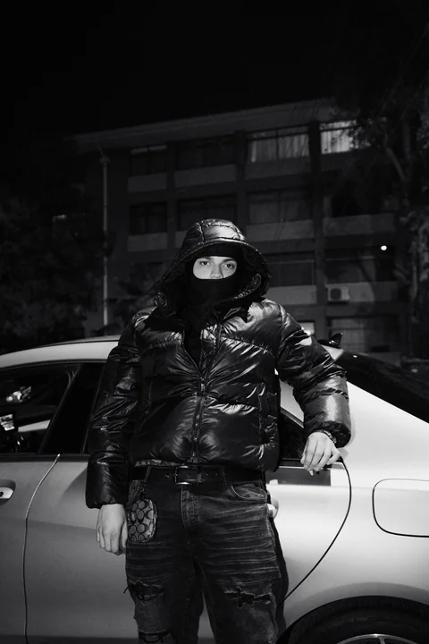 Retrato en blanco y negro de una persona con chaqueta brillante junto a un automóvil