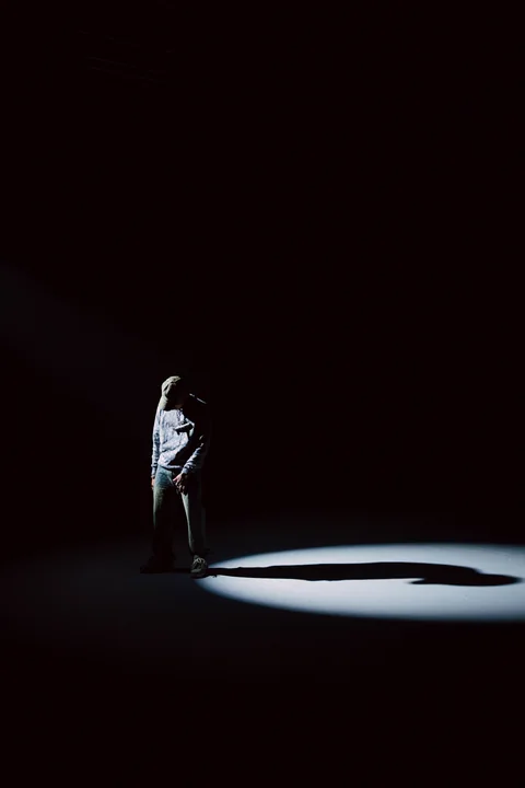 Figura sola bajo un haz de luz, rodeada de espacio oscuro