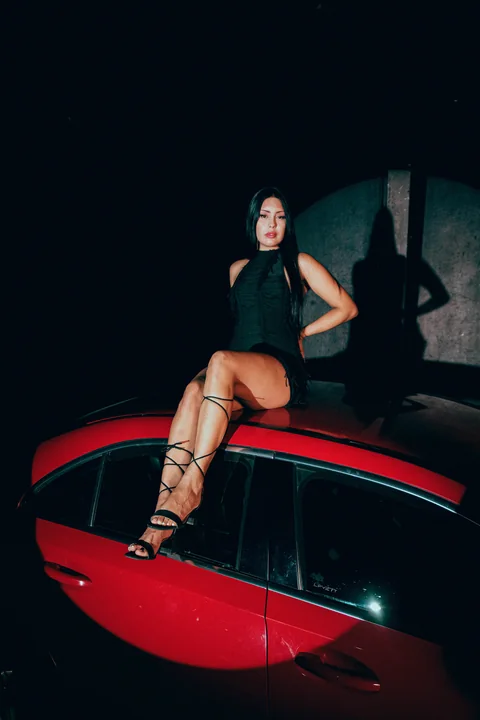 Mujer sentada sobre un automóvil rojo contra la oscuridad