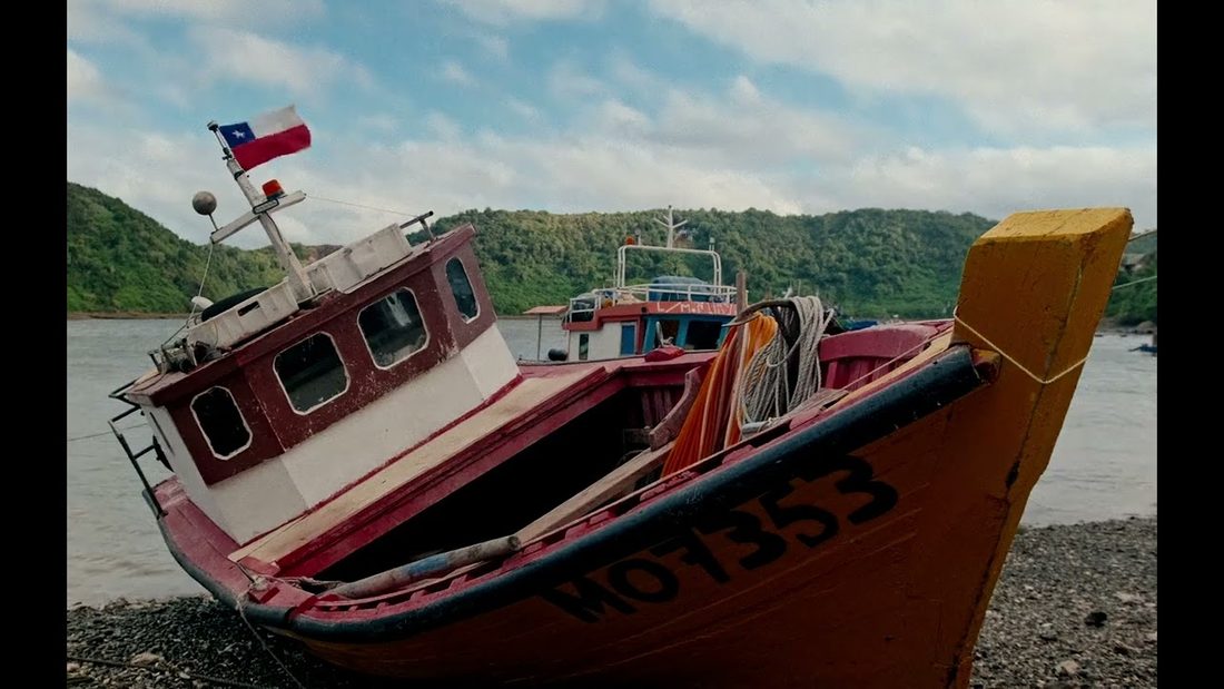 Fotograma de EL SUR DE CHILE ES MÁGICO: bote pesquero rojo con bandera chilena varado en la orilla