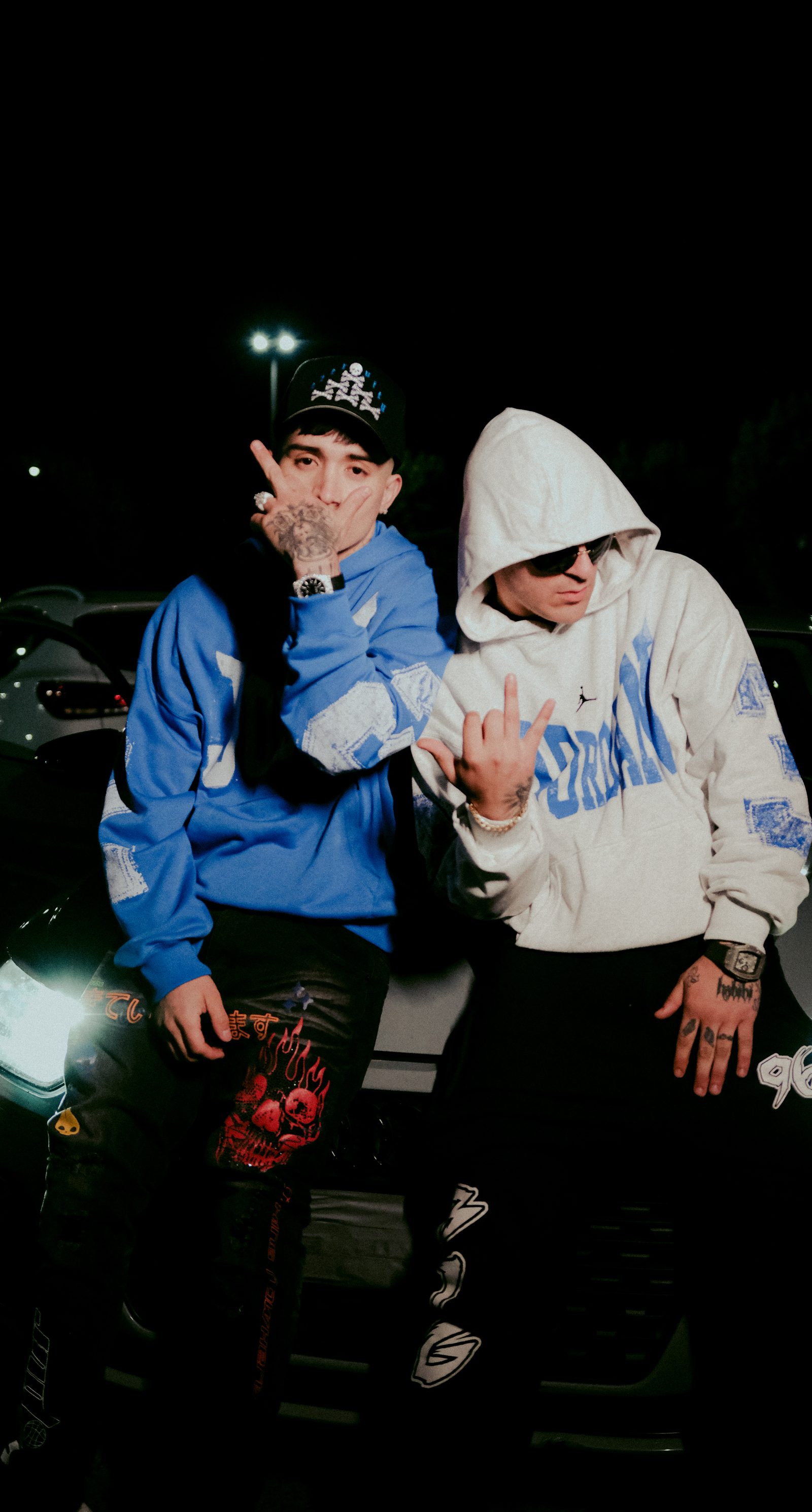 Emiliel y Drago200 de noche en un estacionamiento, con hoodies azul y blanco, set del videoclip La Mental